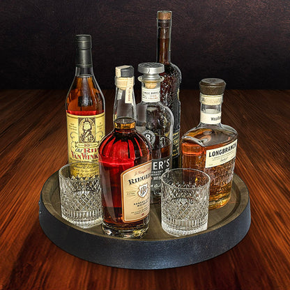 A rustic whiskey display barrel top with a variety of whiskey bottles, glasses, and other accessories arranged on it.
