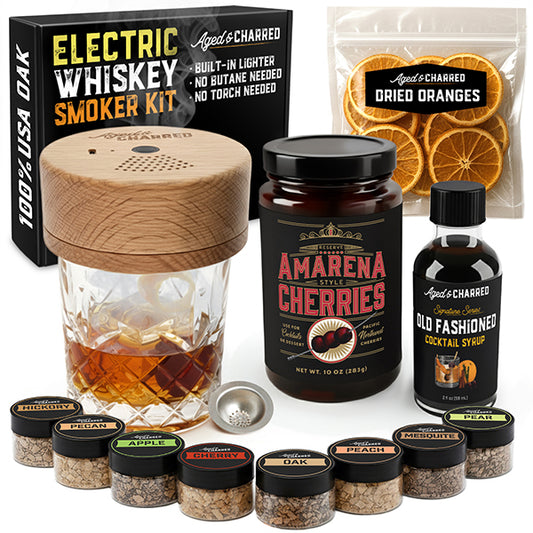 Electric whiskey smoker kit with smoking glass, cherries, oranges, and syrups on a white background